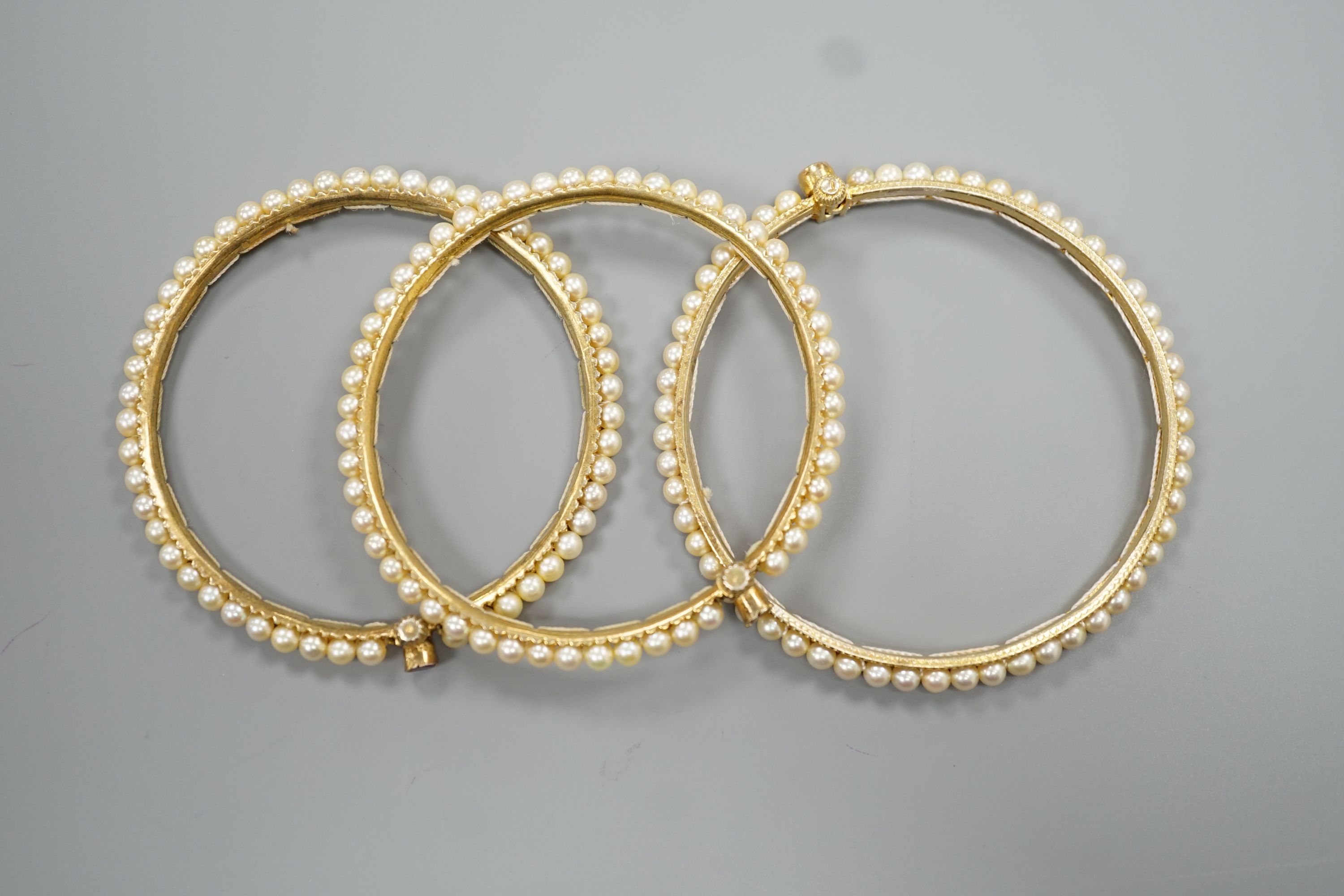 Three gilt white metal and cultured pearl set bangles.